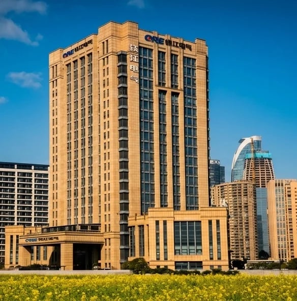 Tall tan brick building with Art Deco architecture, green lawn in foreground, clear blue sky, downtown cityscape in background
